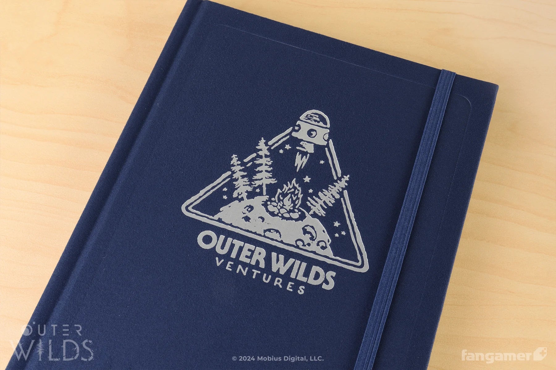 Navy blue notebook with 'Outer Wilds Ventures' logo on a wooden surface